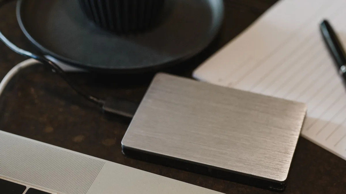 An external hard drive connected to a laptop on a desk, with a notepad and pen nearby